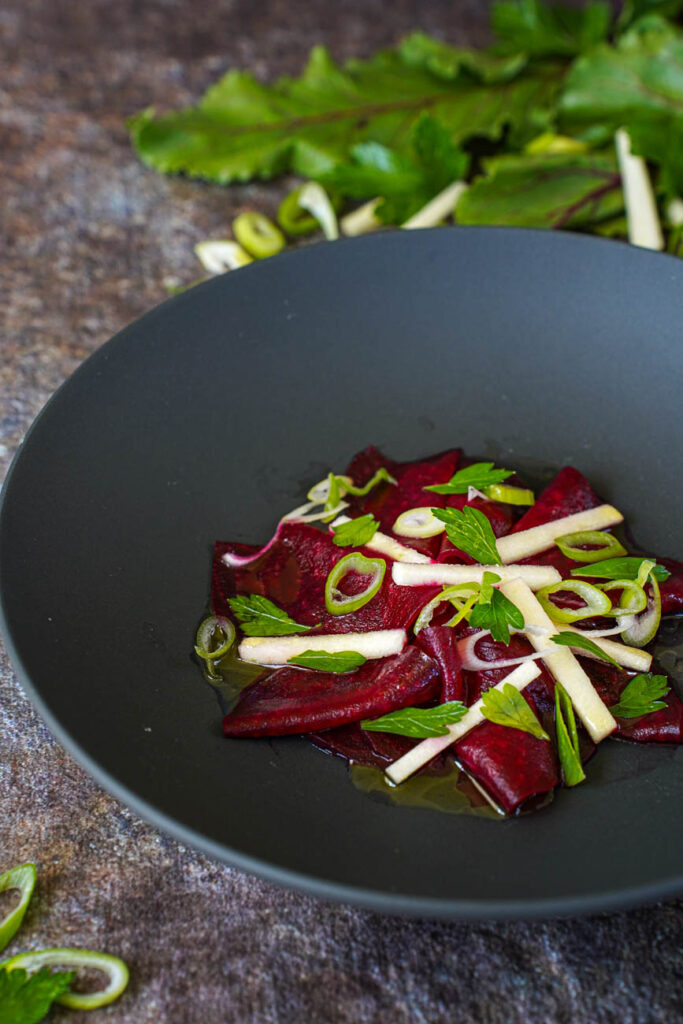 Tangy Beetroot Salad in a black bowl with beet leaves in the background.