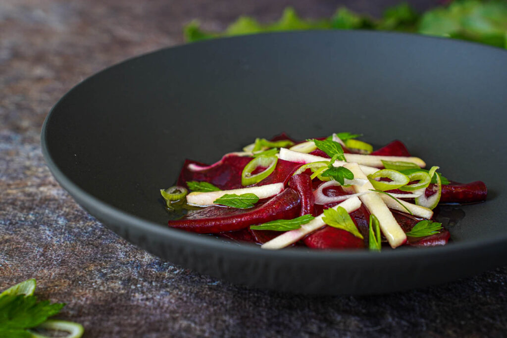 Tangy Beetroot Salad in a black bowl with parsley leaves and slices scallions.