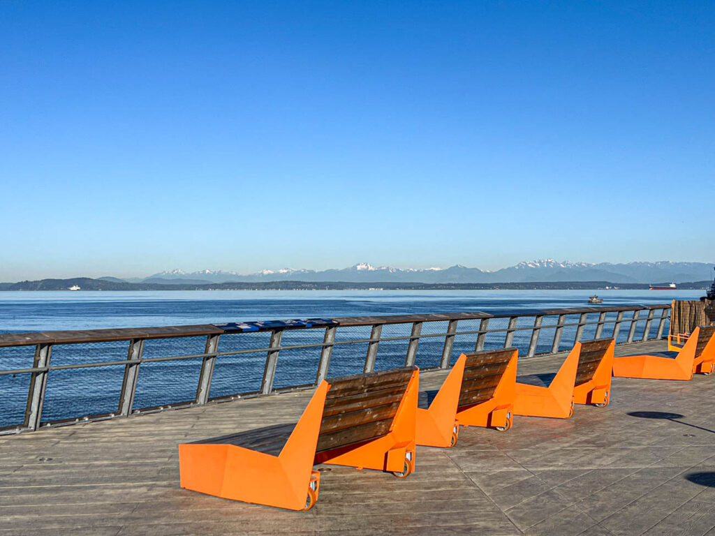 Orange benches in front of water and mountains in Seattle.