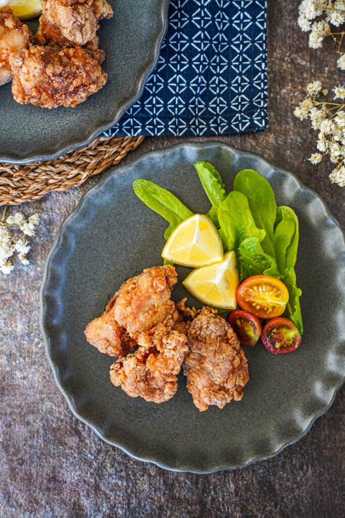 Aerial view of Tatsutaage (Marinated Fried Chicken) on two plates next to white flowers.