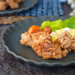 Three Tatsutaage (Marinated Fried Chicken) on a grey plate with lettuce, lemon, and cherry tomatoes.