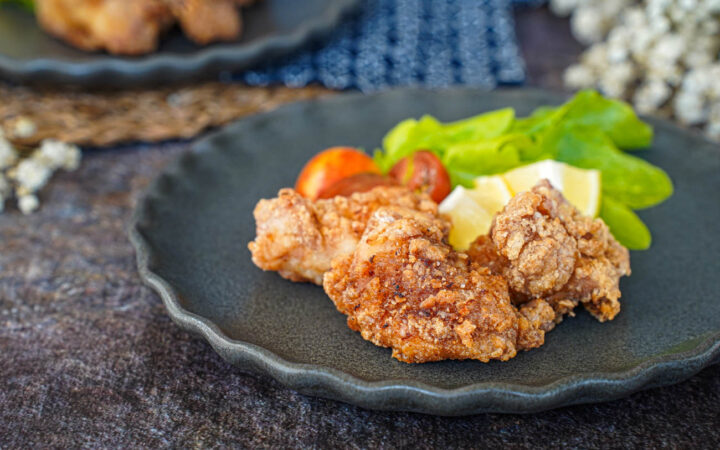Three Tatsutaage (Marinated Fried Chicken) on a grey plate with lettuce, lemon, and cherry tomatoes.