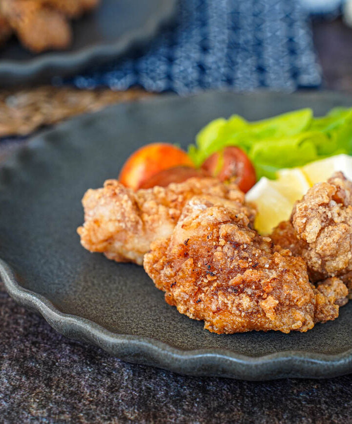 Three Tatsutaage (Marinated Fried Chicken) on a grey plate with lettuce, lemon, and cherry tomatoes.