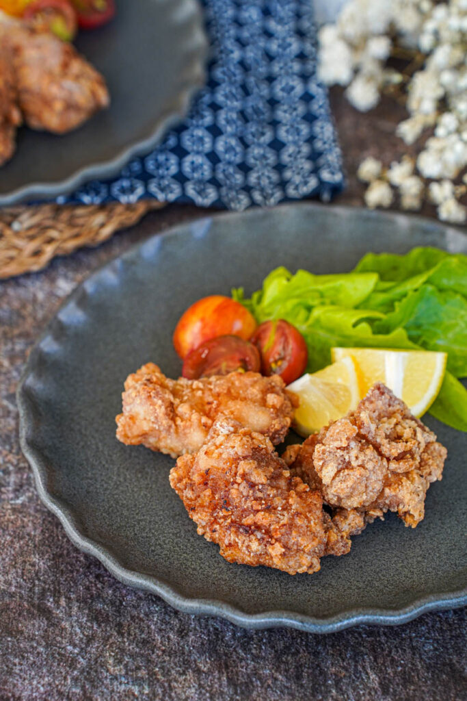 Close up of Tatsutaage (Marinated Fried Chicken) on two plates with lettuce, cherry tomatoes, and lemon wedges.